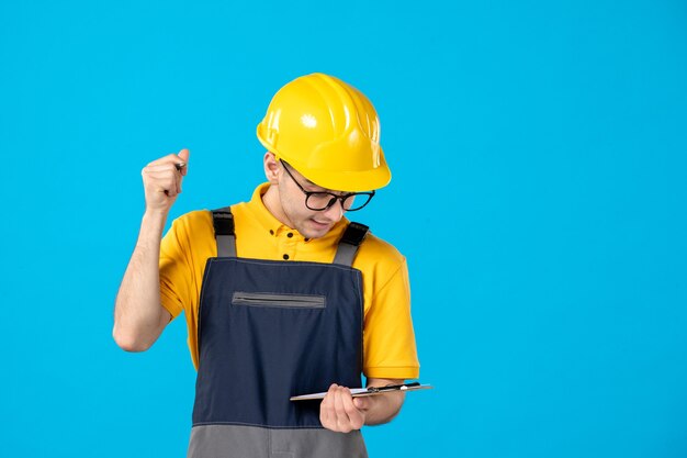 Vorderansicht des männlichen Baumeisters in der Uniform und im Helm, die Notizen auf der blauen Wand machen