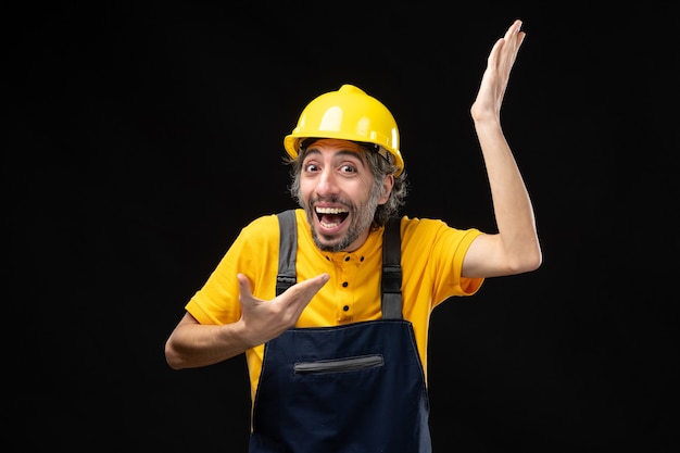 Vorderansicht des männlichen Baumeisters in gelber Uniform an der schwarzen Wand