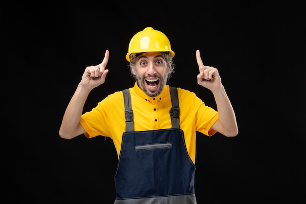 Kostenloses Foto vorderansicht des männlichen baumeisters in gelber uniform an der schwarzen wand