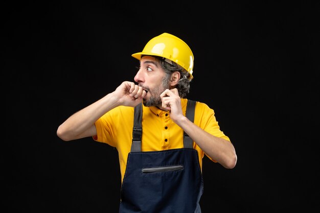 Vorderansicht des männlichen Baumeisters in gelber Uniform an der schwarzen Wand