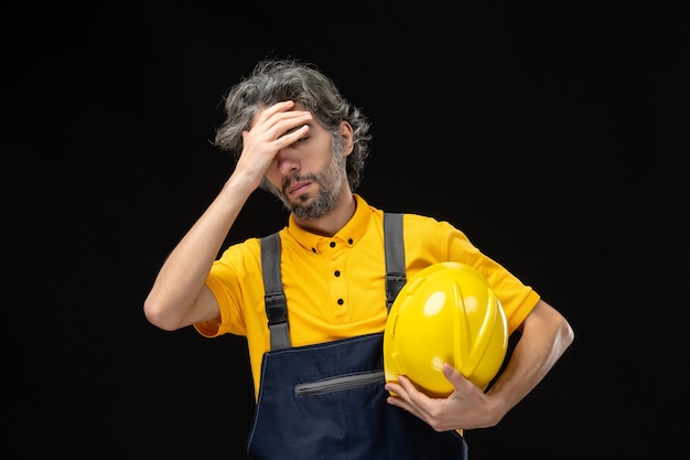 Vorderansicht des männlichen Baumeisters in gelber Uniform an der schwarzen Wand