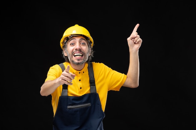 Vorderansicht des männlichen Baumeisters in gelber Uniform an der schwarzen Wand