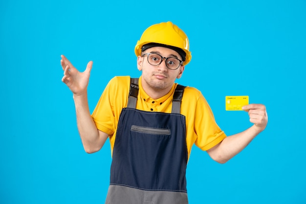 Vorderansicht des männlichen Baumeisters in Uniform mit Kreditkarte auf blauer Wand