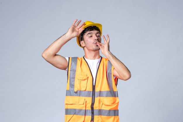 Vorderansicht des männlichen baumeisters in uniform mit schutzhelm auf weißer wand