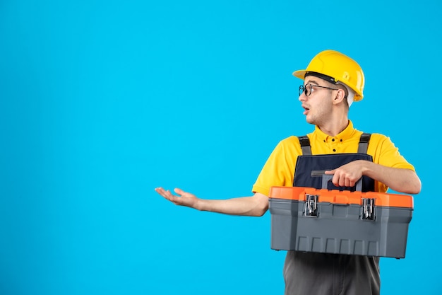 Vorderansicht des männlichen Baumeisters in Uniform mit Werkzeugkasten auf blauer Wand