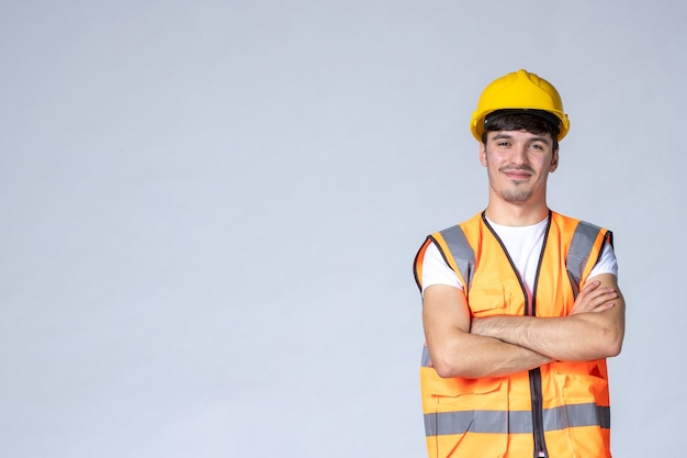 Vorderansicht des männlichen Baumeisters in Uniform und gelbem Helm auf weißer Wand