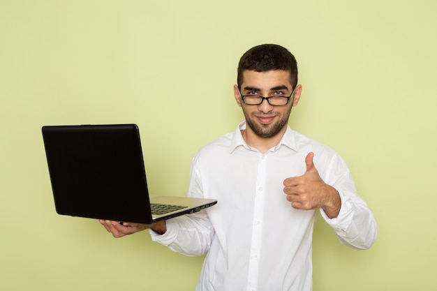 Vorderansicht des männlichen Büroangestellten im weißen Hemd, das Laptop auf hellgrüner Wand hält