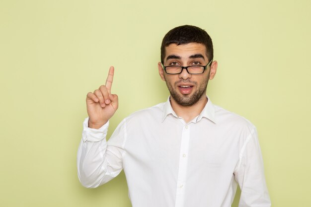 Vorderansicht des männlichen Büroangestellten im weißen Hemd, das mit erhöhtem Finger auf hellgrüner Wand aufwirft