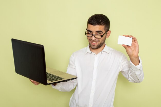 Vorderansicht des männlichen Büroangestellten im weißen Hemd, das seinen Laptop und Karte an der grünen Wand hält