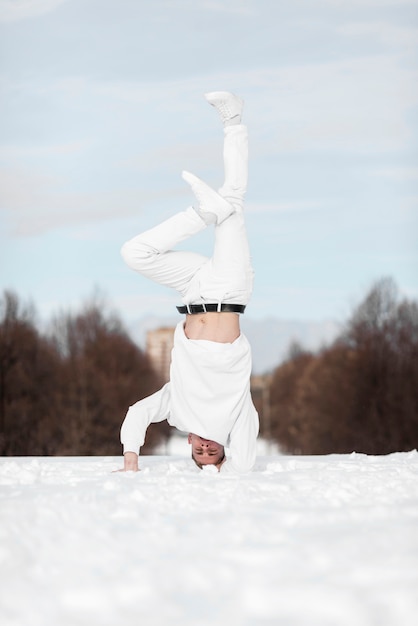 Vorderansicht des männlichen Hip-Hop-Darstellers, der auf Kopf im Schnee steht