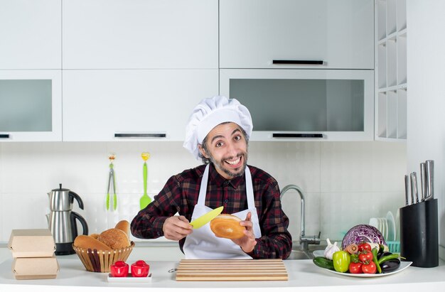 Vorderansicht des männlichen Kochs, der in der Küche Brot mit gelbem Messer schneidet