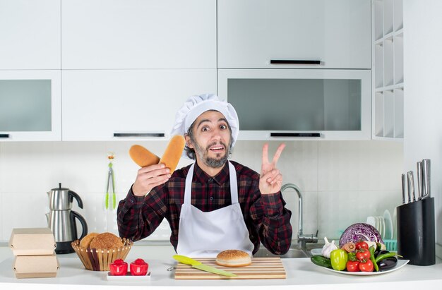 Vorderansicht des männlichen Kochs, der Victory-Zeichen mit Brot in der Küche macht