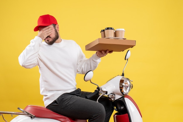 Vorderansicht des männlichen Kuriers, der Lieferkaffee und Essen auf gelber Wand hält