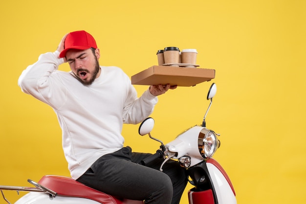 Vorderansicht des männlichen Kuriers, der Lieferkaffee und Essen auf gelber Wand hält