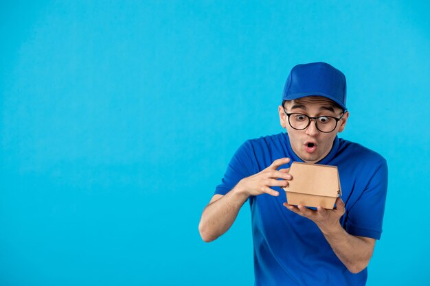 Vorderansicht des männlichen Kuriers in der blauen Uniform mit der kleinen Nahrungsverpackung auf Blau