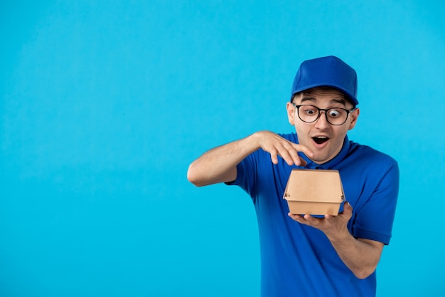 Vorderansicht des männlichen Kuriers in der blauen Uniform mit der kleinen Nahrungsverpackung auf Blau