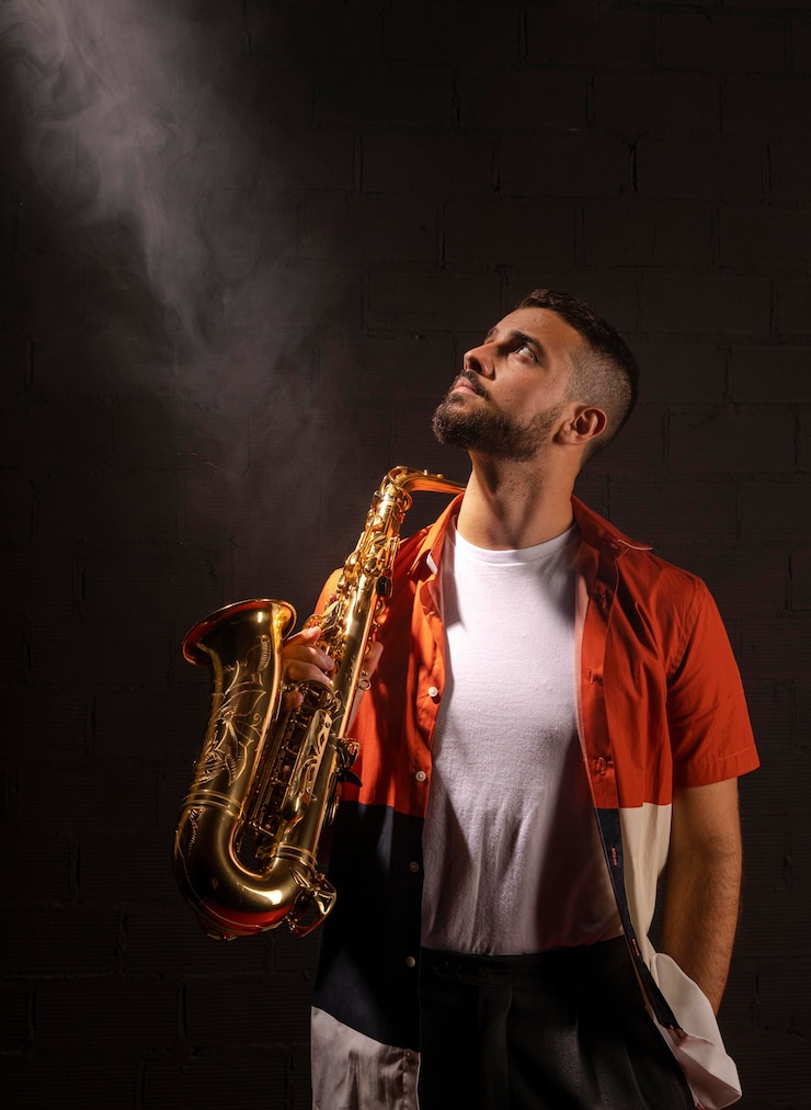 Kostenlose Foto vorderansicht des männlichen musikers, der in richtung scheinwerfer schaut, während saxophon hält