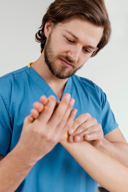 Vorderansicht des männlichen osteopathischen Therapeuten, der das Handgelenk der Patientin prüft