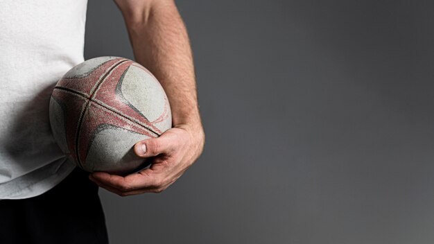 Vorderansicht des männlichen Rugbyspielers, der Ball neben Hüfte mit Kopienraum hält