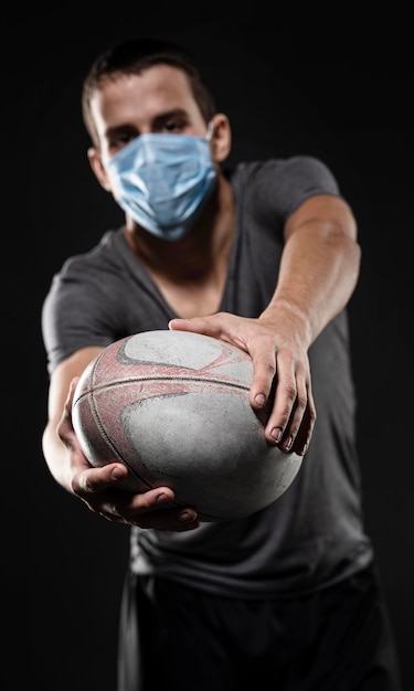 Vorderansicht des männlichen Rugbyspielers mit der medizinischen Maske, die Ball hält