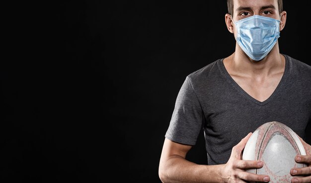 Vorderansicht des männlichen Rugbyspielers mit medizinischer Maske und Kopienraum