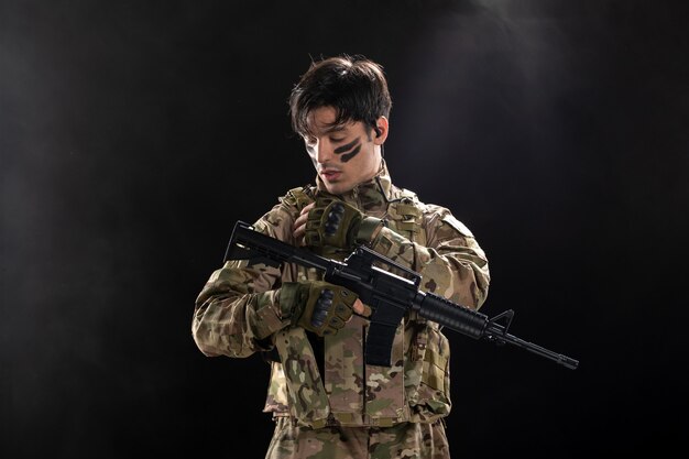 Vorderansicht des männlichen Soldaten in Tarnung mit dunkler Wand des Maschinengewehrs
