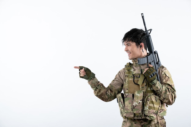 Kostenloses Foto vorderansicht des männlichen soldaten mit maschinengewehr in der weißen wand der tarnung