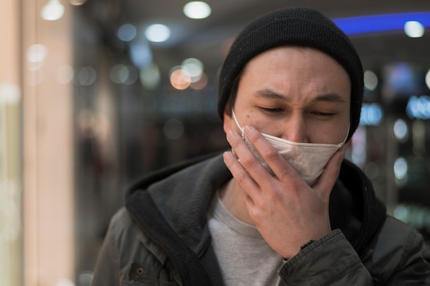 Vorderansicht des Mannes am Einkaufszentrum, das in der medizinischen Maske hustet