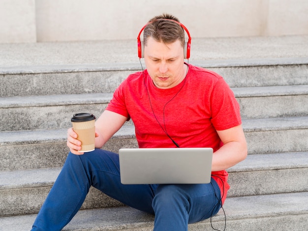 Vorderansicht des Mannes auf Stufen, die Kaffee trinken und am Laptop arbeiten