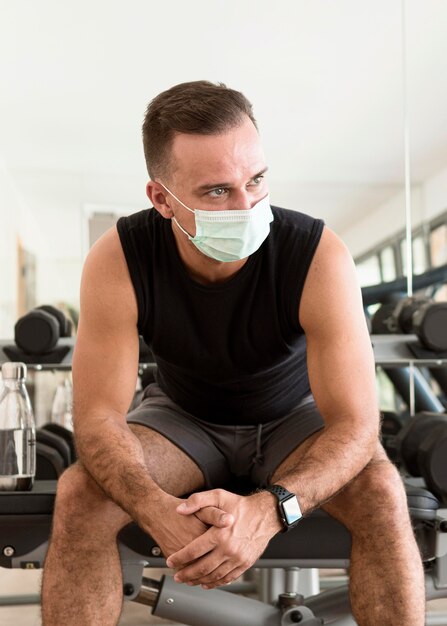 Vorderansicht des Mannes im Fitnessstudio mit medizinischer Maske