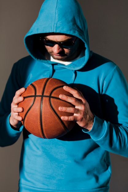 Vorderansicht des Mannes im Hoodie und in Sonnenbrille, die Basketball halten