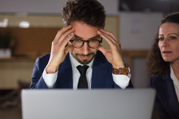 Vorderansicht des müden Mannes in den Brillen, die Laptop betrachten