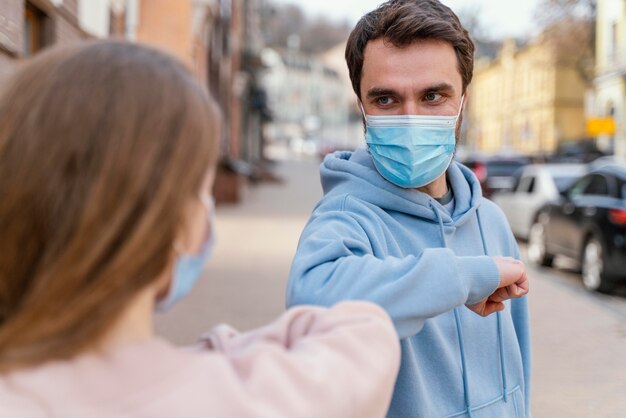 Vorderansicht des Paares mit medizinischer Maske unter Verwendung des Ellbogengrußes