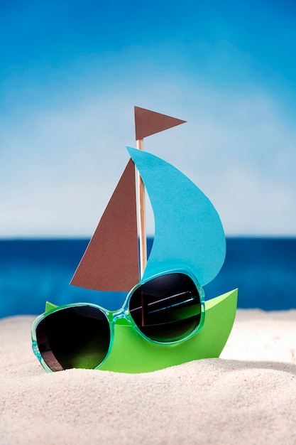 Kostenloses Foto vorderansicht des papierboots auf strandsand mit sonnenbrille