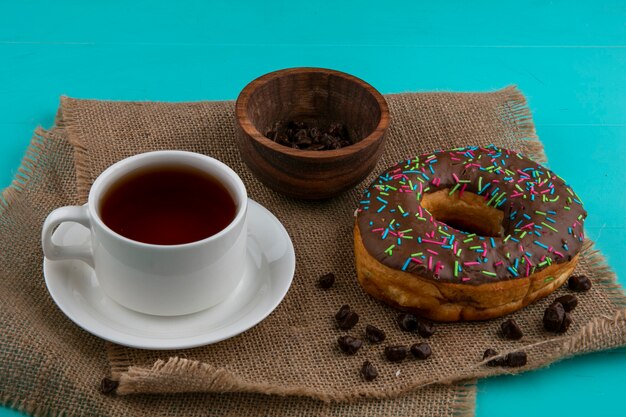 Vorderansicht des Schokoladendonuts mit einer Tasse Tee und Pralinen auf einer beigen Serviette