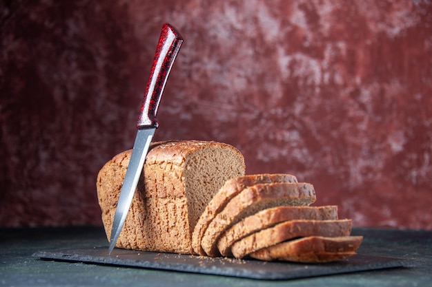 Vorderansicht des Schwarzbrotscheibenmessers auf dunklem Farbbrett auf gemischtem, beunruhigtem Hintergrund