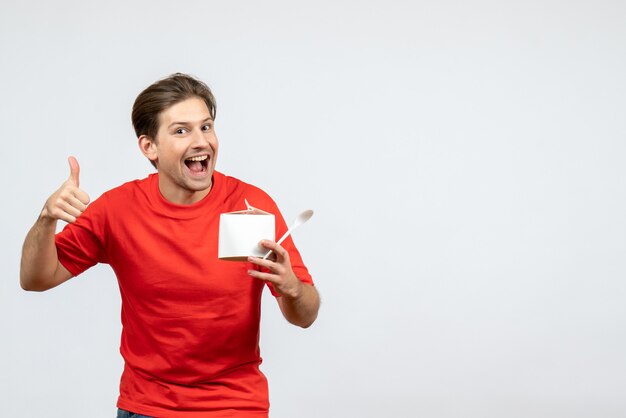 Vorderansicht des selbstbewussten jungen Mannes in der roten Bluse, die Papierbox hält und ok Geste auf weißem Hintergrund macht