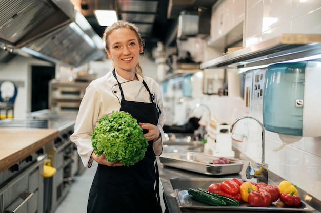 Kostenloses Foto vorderansicht des smiley-köchin in der küche, die salat hält