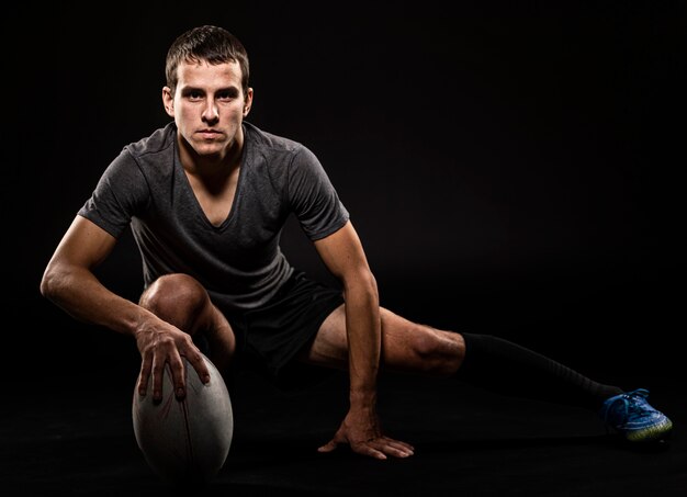 Vorderansicht des sportlichen gutaussehenden Rugbyspielers, der Ball mit Kopienraum hält