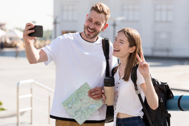 Vorderansicht des Touristenpaares draußen mit Rucksäcken und Karte, die selfie nehmen