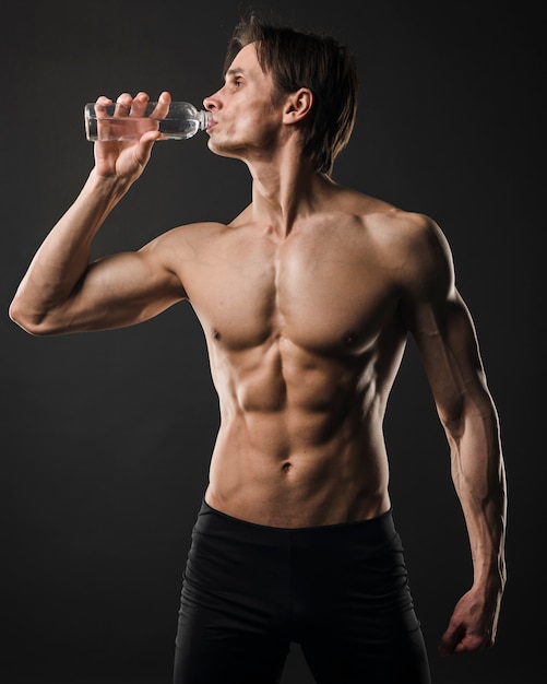 Vorderansicht des Trinkwassers des athletischen hemdlosen Mannes von der Flasche