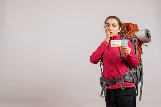 Vorderansicht des verwirrten jungen Reisenden mit großem Rucksack, der Reiseticket mit freiem Raum hält