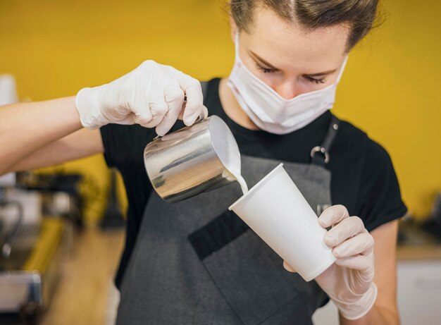 Vorderansicht des weiblichen Barista, der Milch in Kaffeetasse gießt