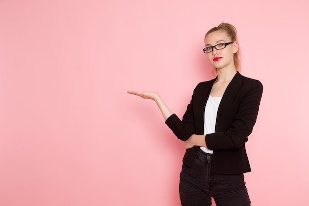 Vorderansicht des weiblichen Büroangestellten in der schwarzen strengen Jacke, die gerade auf der rosa Wand aufwirft