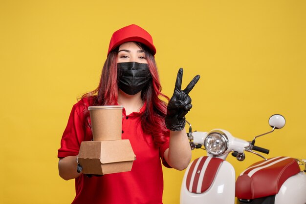 Vorderansicht des weiblichen Kuriers in der Maske mit Liefernahrung auf gelber Wand