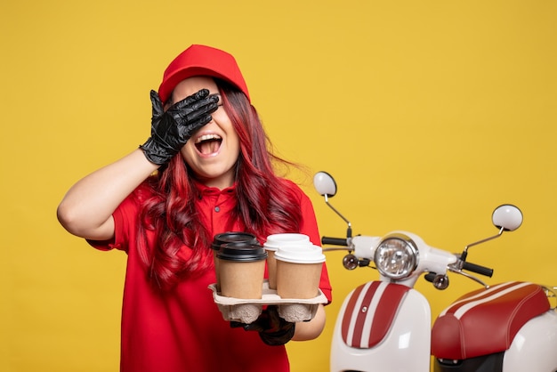 Vorderansicht des weiblichen Kuriers in der roten Uniform mit Kaffee auf gelber Wand