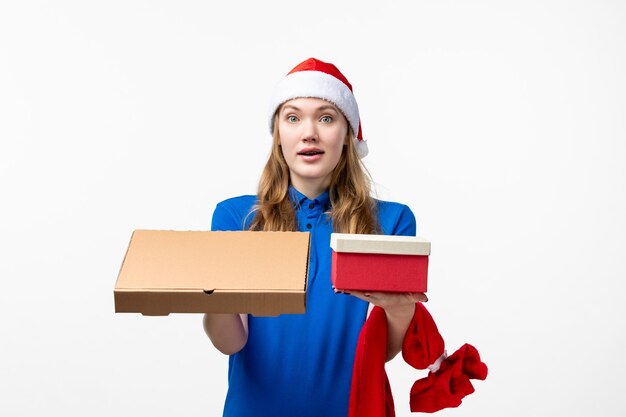 Vorderansicht des weiblichen Kuriers mit Lebensmittelbox und Geschenk auf weißer Wand