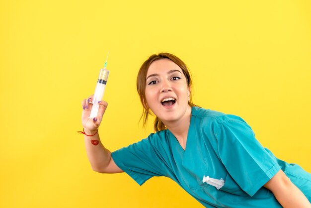 Vorderansicht des weiblichen Tierarztes, der große Injektion auf gelber Wand hält