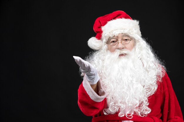Vorderansicht des Weihnachtsmannes im klassischen roten Anzug mit weißem Bart an der schwarzen Wand