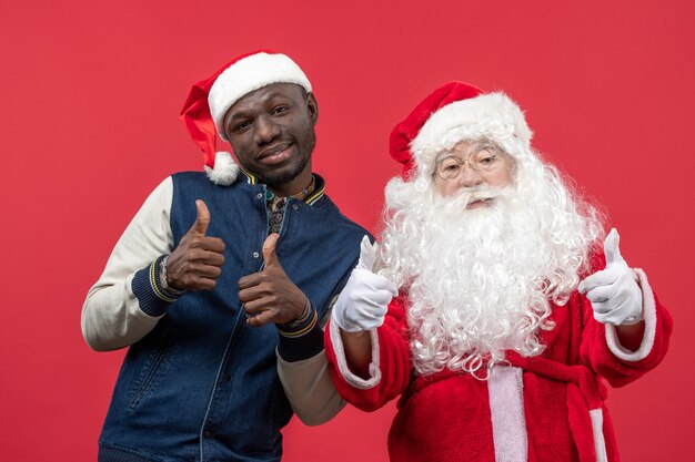 Vorderansicht des Weihnachtsmannes mit dem jungen Mann an der roten Wand